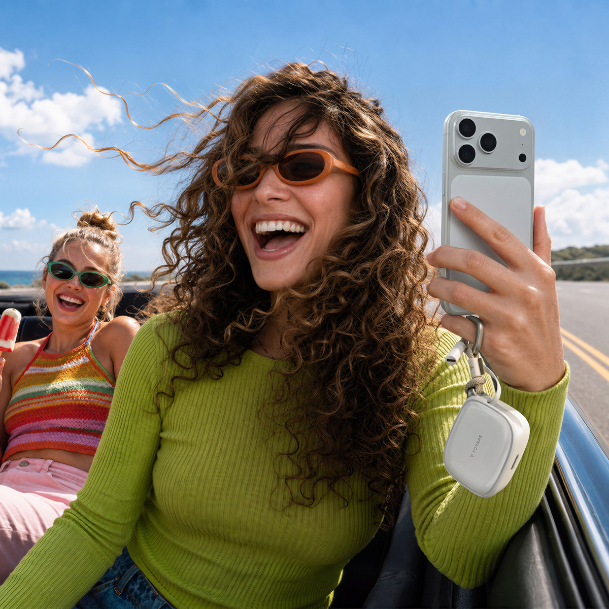 Woman in a convertible holding an iPhone with a white TORRAS PackGo Cube 10K power bank hanging from it