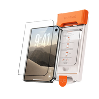 A screen protector and the orange TORRAS auto-dust installation frame standing beside the phone they fit, a desert mountain wallpaper on screen