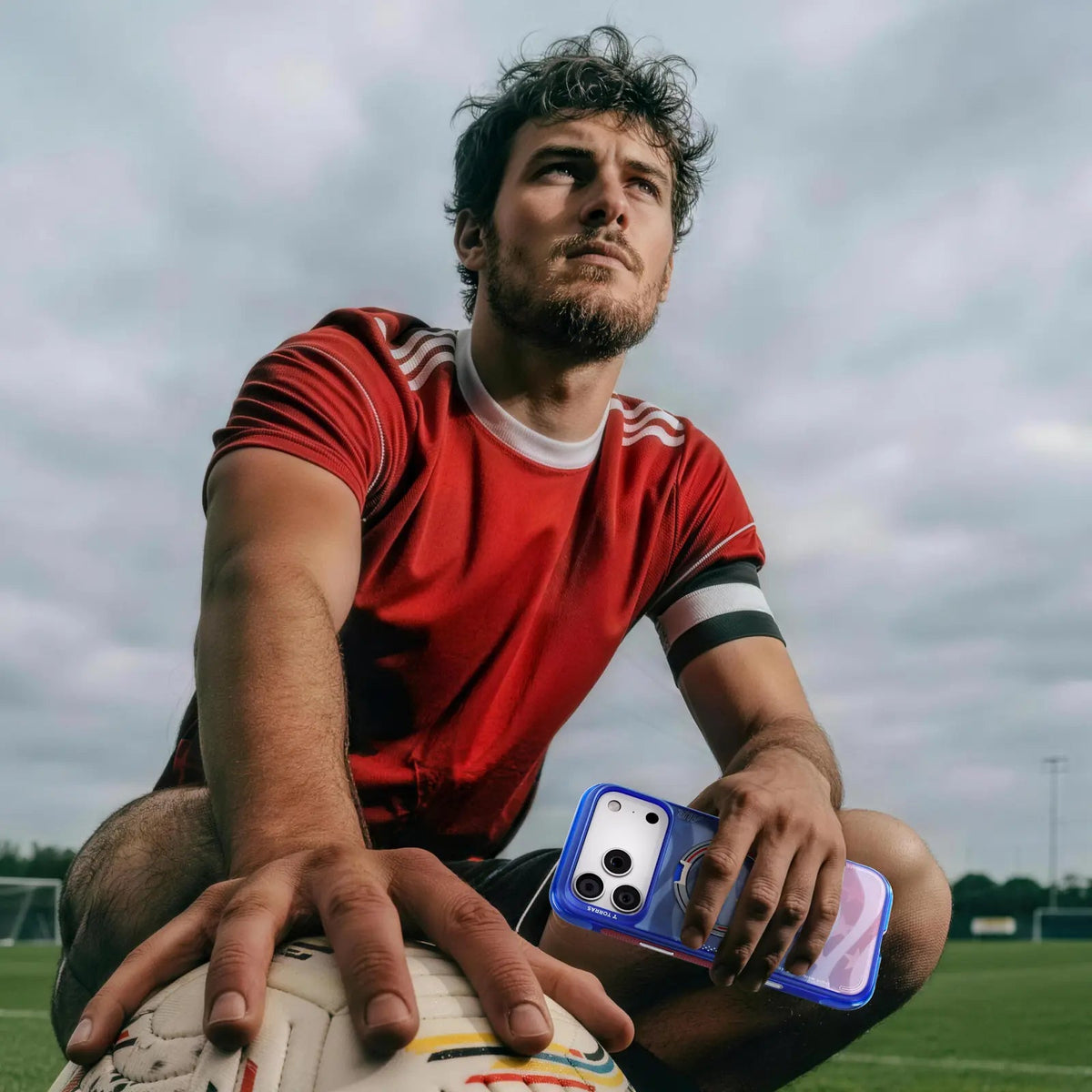 Footballer in a red kit on the pitch holding an iPhone 18 Pro Max in the blue-violet Football case