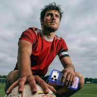 Footballer in a red kit on the pitch holding an iPhone 18 Pro Max in the blue-violet Football case