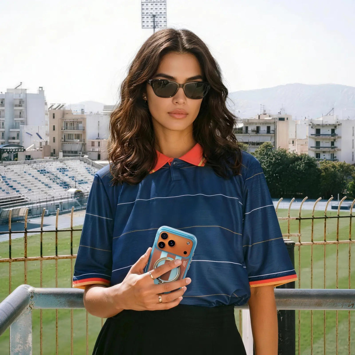Woman in a navy striped football shirt at a stadium, holding an iPhone in the pale blue Football case