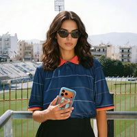 Woman in a navy striped football shirt at a stadium, holding an iPhone in the pale blue Football case