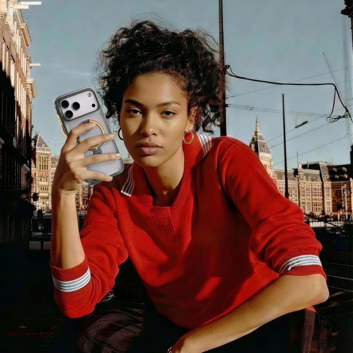 Woman in a red sweatshirt in a city square, holding an iPhone in the clear Football case with a red-yellow ring