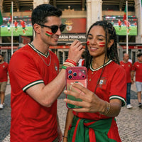 Two Portugal fans in red kits outside a stadium, one holding an iPhone in the pink FPF case