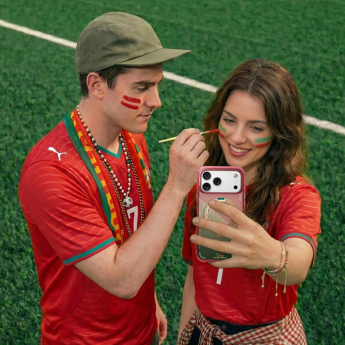 Portugal fans on the pitch painting face stripes, holding an iPhone in the pink FPF case